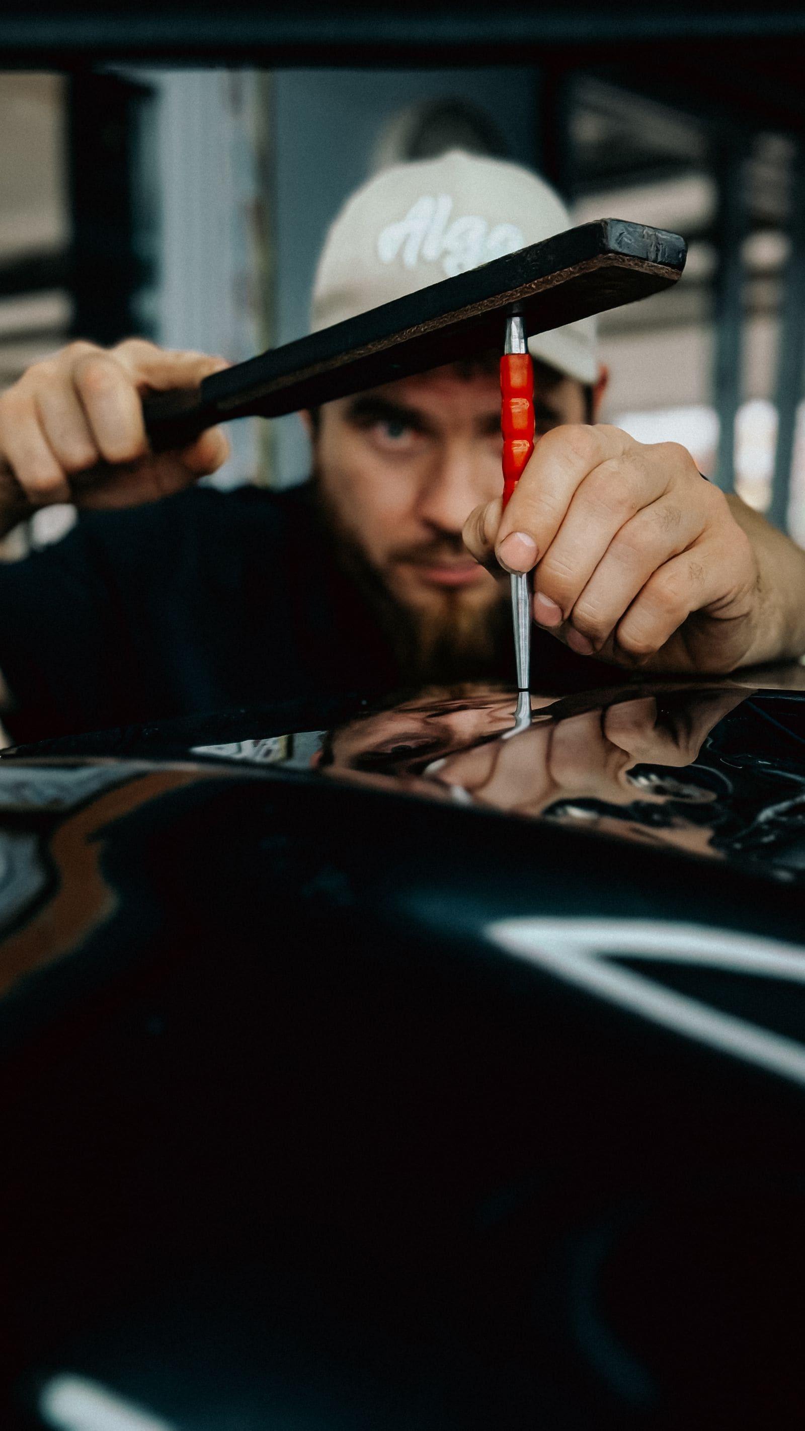 A panel beater working a dent out of a car body panel with a hand tool