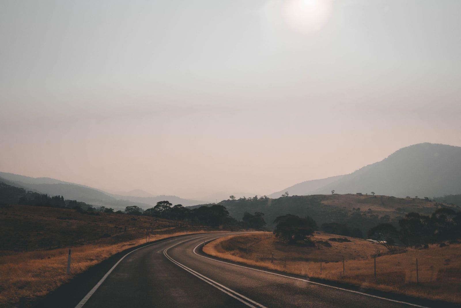 An open two-lane country road curving through dry grass and gum trees in regional NSW